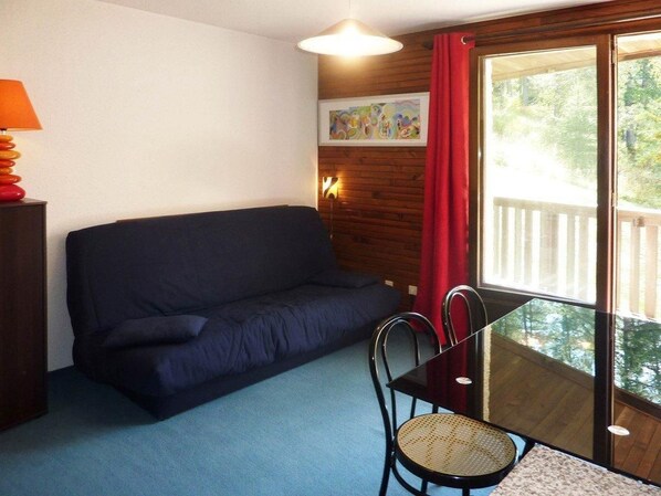A room with a dark blue sofa, a small round table with a chair, a lamp, and a painting on the wall.