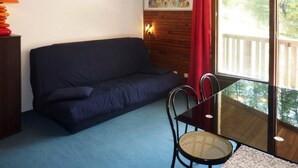 A room with a dark blue sofa, a glass table with two chairs, a lamp, a painting on the wall, and a window with a red curtain. - 300m from ski slopes, 2nd floor, view forest, balcony, tv, ski locker, 24m², Les Orres (Les Orres)
