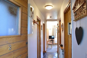A narrow hallway with wooden walls, a window with a grid pattern, and a television in the distance.