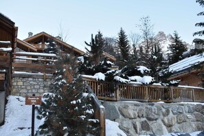 A wooden chalet with stone walls, snow-covered roofs, and a sign indicating a 'Chemin de TARA' pathway.