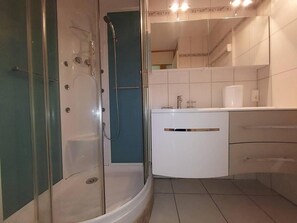 Een moderne badkamer met een douchecabine van glas, een wit wastafelmeubel met een spiegel, en betegelde vloer.