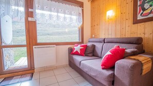 A cozy room with a brown sofa, a window with curtains, a radiator, and a wooden wall with a light fixture. - View ski slopes, terrace, tv, ski locker, 42m², Valmorel (Valmorel)