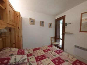 Een slaapkamer met een houten garderobe, een bed met een sprei, een stoel en een deur die leidt naar een andere kamer.