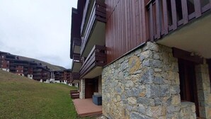 A modern building with stone walls and wooden balconies, set on a grassy slope with other buildings in the background. - View ski slopes, terrace, tv, ski locker, 42m², Valmorel (Valmorel)