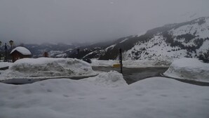 Schneebedeckte Landschaft mit einem kleinen Gebäude, einem Parkplatzschild und einem Berg im Hintergrund.