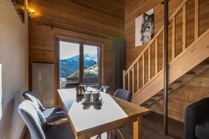Ein Interieur einer Holzhütte mit einem Esstisch, Stühlen, Blick auf Berge und einer Treppe.