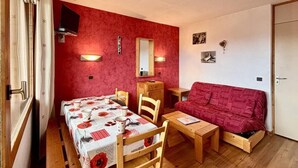 Une pièce chaleureuse avec une table à manger dressée pour deux personnes, un canapé rouge et un petit meuble en bois.