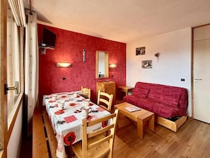 Una stanza accogliente con un tavolo da pranzo apparecchiato per due persone, un divano rosso e un piccolo mobiletto in legno.
