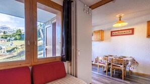 A cozy room with a red sofa, a dining table with chairs, and a view of a mountainous landscape through a window. - Ski-in/ski-out & foot of the slopes, 2nd floor, view ski slopes, terrace, tv, 24m² (Bellentre)