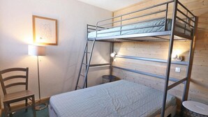 Ein Schlafraum mit Etagenbetten, einem Holzvorhang, einem Schreibtisch mit Stuhl und einer Lampe.