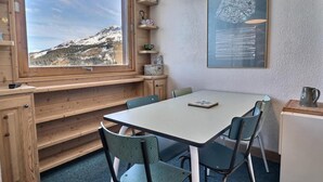 Ein gemütliches Zimmer mit großem Fenster und Blick auf die Berge, einer Holzbank, einem Tisch mit Stühlen und einer Wandlampe.