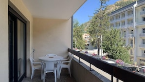 A balcony with a table and chairs, overlooking a residential area with buildings and trees. - 150m from resort center, 1st floor, balcony, tv, 26m², Brides Les Bains (Brides-les-Bains)