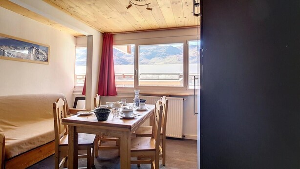 Een gezellige kamer met een houten plafond, een eettafel gedekt met borden en kopjes, een bank en een raam met uitzicht op bergen.