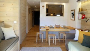 A cozy living room with a wooden floor, a sofa, a dining area with stools, and a kitchen visible through an archway. - 10m from ski slopes, 1st floor, view ski slopes, balcony, 40m², Méribel-Mottaret (Méribel - Les Allues)