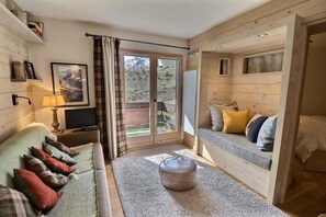 A cozy room with a sofa, a television, a window with curtains, and a view of the outdoors.