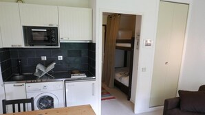 A compact kitchen with a microwave, washing machine, and a small dining table with a decorative item. A bunk bed is visible in the adjacent room. - Ground floor, balcony, parking, tv, ski locker, 20m², Valloire (Valloire)
