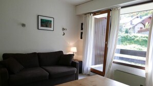 A room with a dark brown sofa, a wooden table with a spherical object on it, a small lamp, and a window with curtains. - Ground floor, balcony, parking, tv, ski locker, 20m², Valloire (Valloire)