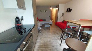 Een kleine keuken met een fornuis, een eethoek met een tafel en stoelen, en een rode bank op de achtergrond.