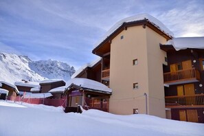 Un bâtiment enneigé, doté d’un balcon, avec une chaîne de montagnes en arrière-plan.