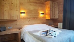 Um quarto tipo cabana de madeira, com uma cama, um criado-mudo e duas luzes fixadas na parede.
