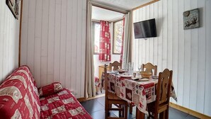 Tunnelmallinen huone, jossa on puulattia, ruokapöytä katettuna lautasilla ja laseilla, punavalkoraiteinen sohva ja seinälle asennettu televisio.