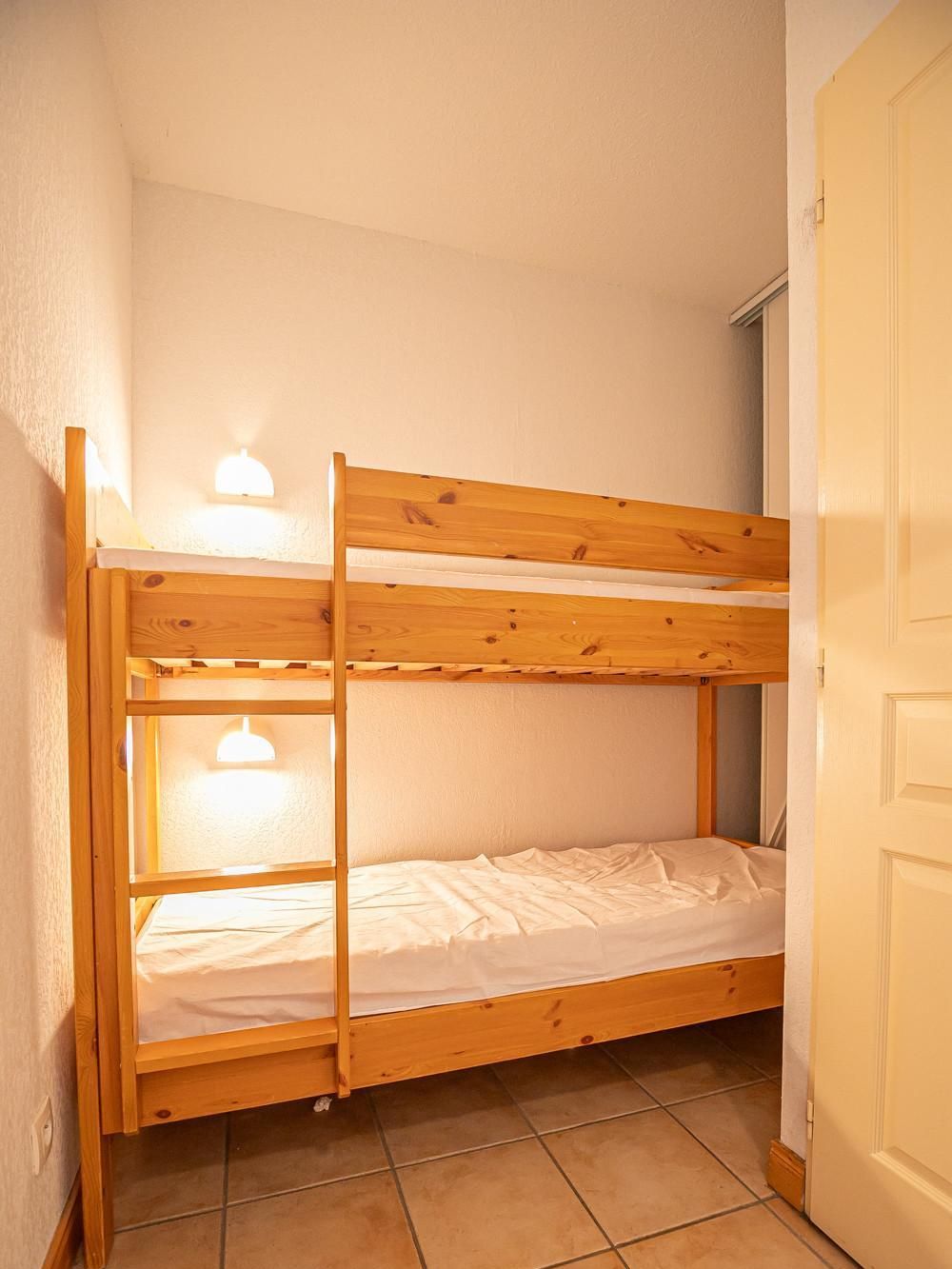 A bunk bed with two levels, a white door, and tiled flooring.