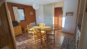 A dining area with a wooden table and chairs, a television on a wooden cabinet, and a window with curtains. - 10m from ski slopes, floor -1, balcony, tv, 31m², Aussois (Aussois)