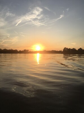 Un coucher de soleil sur une étendue d’eau calme, avec la silhouette d’arbres à l’horizon.