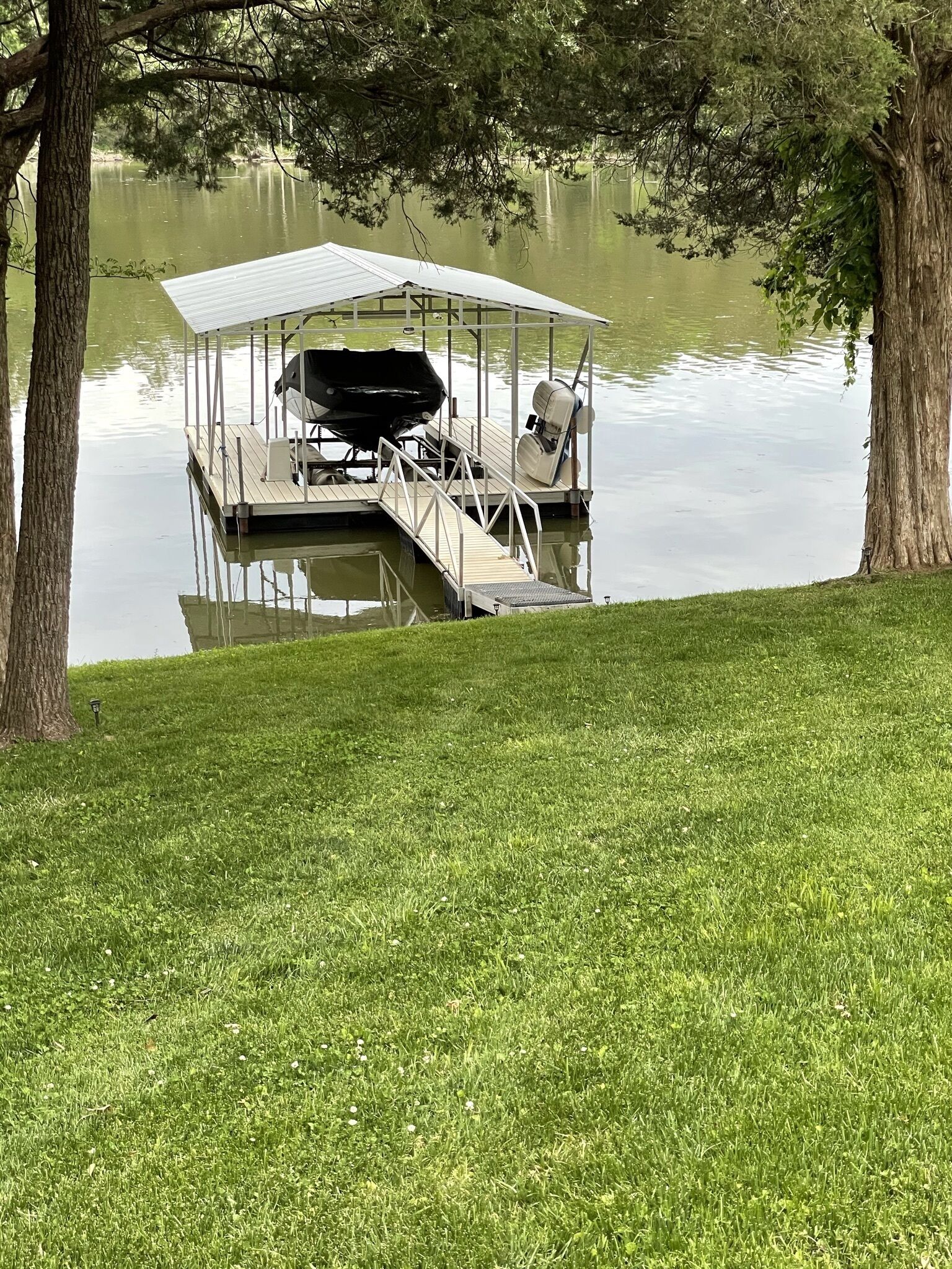 Une jetée dotée d’un espace de repos abrité et d’un barbecue, entourée d’arbres et d’une pelouse.