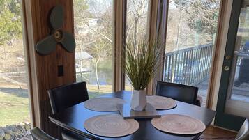 Un coin repas avec une table et des chaises en bois foncé, un ventilateur décoratif et une vue sur un lac, visible à travers de grandes fenêtres.