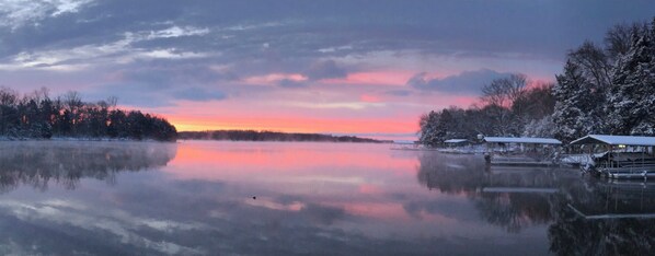 Un lac paisible au coucher du soleil, avec des arbres couverts de neige et une jetée agrémentée de constructions abritées.