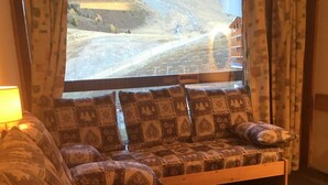 A cozy room with a large window, a wooden bench with patterned cushions, and a lamp on the left. - 10m from ski slopes, 4th floor, view ski slopes, balcony, ski locker, 24m², Les Arcs (Les Arcs)