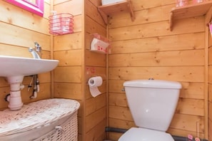 Een houten badkamer met een wastafel, toilet en rieten mand.