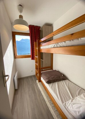 Habitació petita amb literes, finestra amb vista, llum al sostre i una porta.