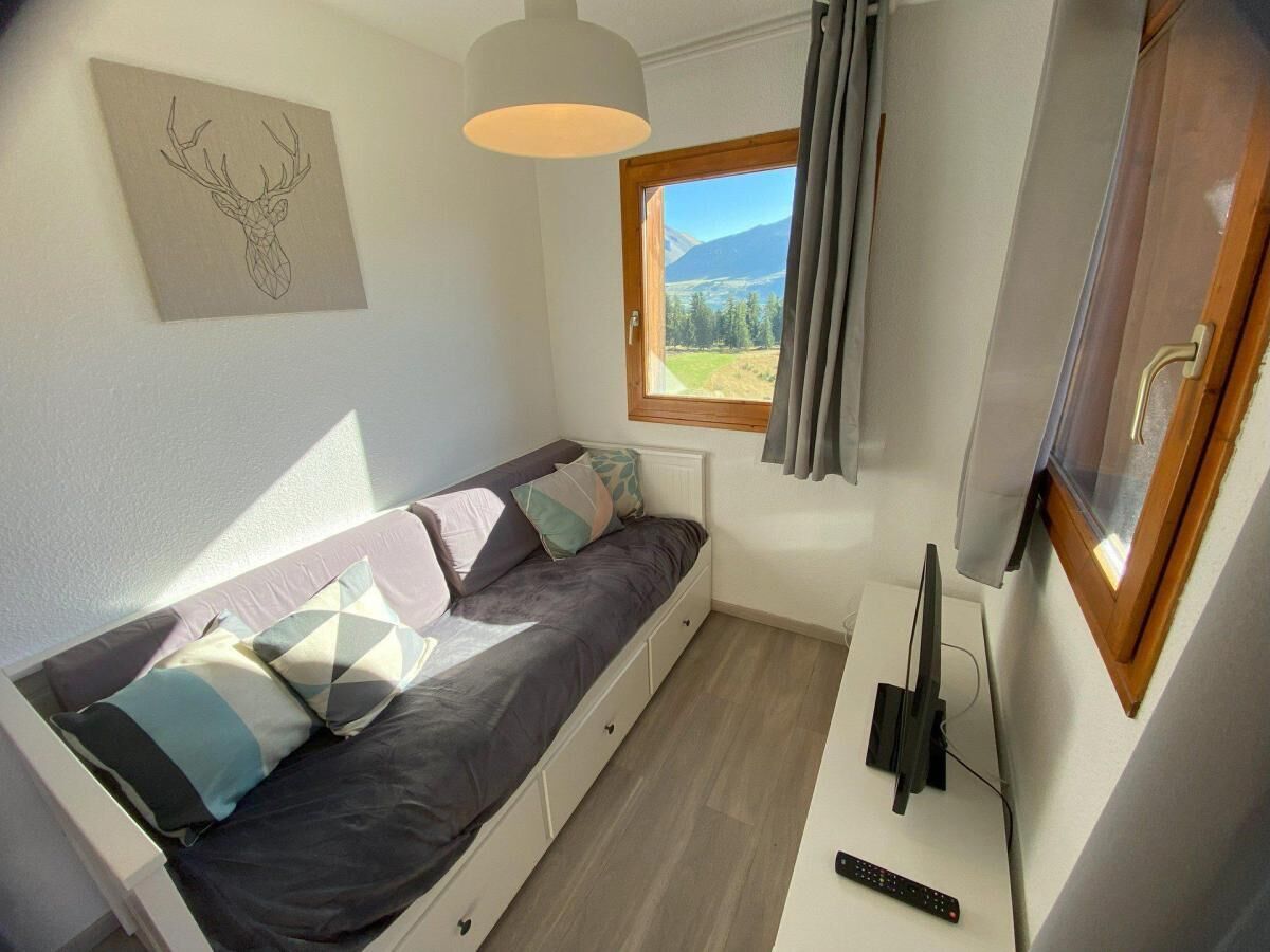 Een knus, klein kamertje met een bed, een raam met uitzicht op bergen, een plafondlamp en een televisie.