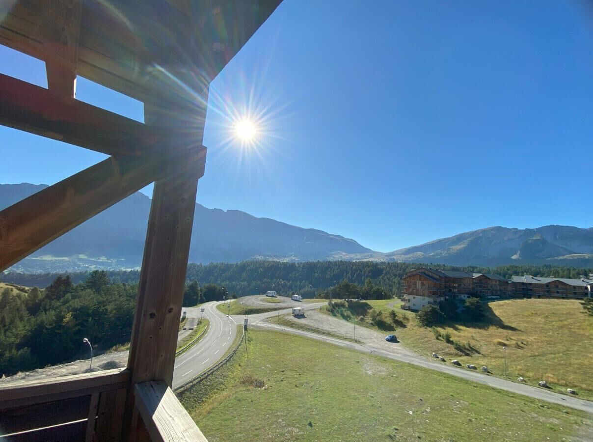 Une vue depuis une structure en bois donnant sur une route, avec une montagne en arrière-plan et un immeuble à plusieurs étages.