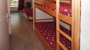 A bunk bed room with a red patterned bedspread, a wooden bunk bed frame, and a door leading to a balcony with a red curtain. - 300m from ski slopes, 5th floor, view forest, balcony, tv, 38m², Les Orres (Les Orres)