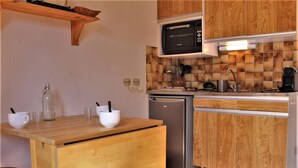 A compact kitchen with wooden cabinets, a built-in microwave, a stainless steel refrigerator, and a small dining area with a wooden table and chairs.