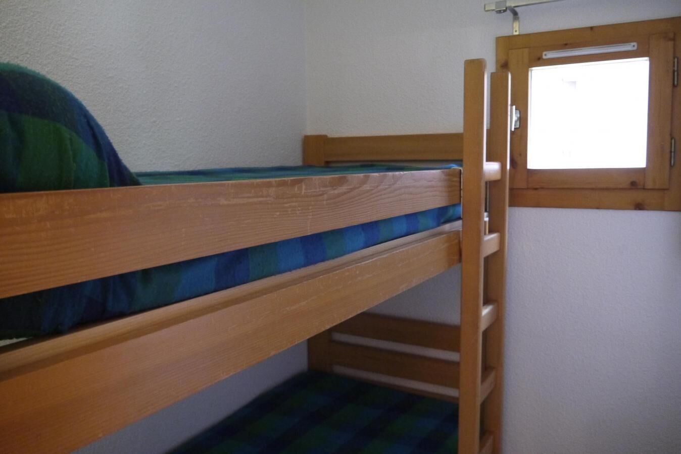 A bunk bed with a window, wooden walls, and a blue checkered blanket.