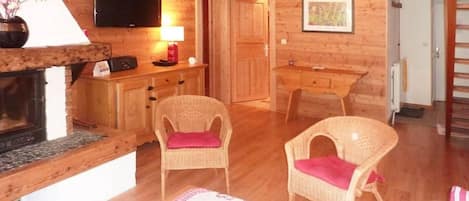 Un interior de madera con chimenea, sillas de mimbre, un televisor de pantalla plana y una puerta que da a otra habitación.