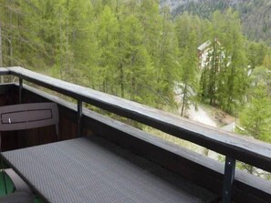 A balcony with a view of a forested area and a building in the distance.