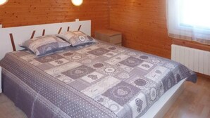 A bedroom with a wooden ceiling, a bed with a patterned bedspread, two bedside lamps, and a window with a sheer curtain.