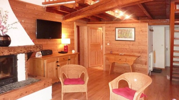 A cozy wooden interior with a fireplace, wicker chairs, a flat-screen TV, and a dining area.