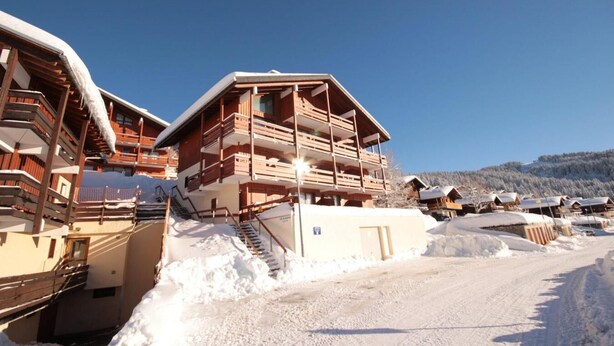 En flerlags trælodge med balkoner, en skilift og et snæret landskab.