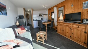 En kompakt opholdsstue med sofa, spisebord, fjernsyn og træskabe.