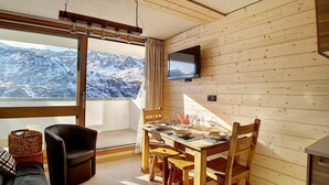 A cozy room with a wooden interior, a dining table set for four, a TV mounted on the wall, and a large window offering a mountain view. - Ground floor, view exceptional, balcony, tv, ski locker, 24m², Les Menuires (Les Menuires)
