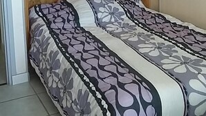 Sängyssä on kukkakuviollinen päiväpeite, sydämenmuotoisia aukkoja sisältävä puinen pääty ja sängyn yläpuolella oleva puinen vaatekaappi.