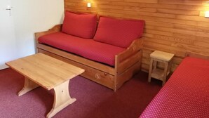 A wooden sofa with red cushions, a wooden table, and a small wooden stool in a room with wooden walls and a red carpet. - 26m from ski slopes, 2nd floor, balcony, tv, ski locker, 35m², Valmorel (Valmorel)