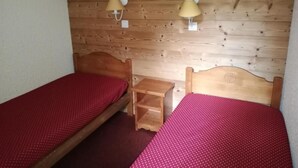 A small, cozy room with two wooden beds, each with a red bedspread. There are two wall-mounted lamps and a small wooden nightstand between the beds. - 26m from ski slopes, 2nd floor, balcony, tv, ski locker, 35m², Valmorel (Valmorel)