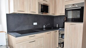 A modern kitchen with light wood cabinets, a black countertop, a microwave, an oven, and a sink.